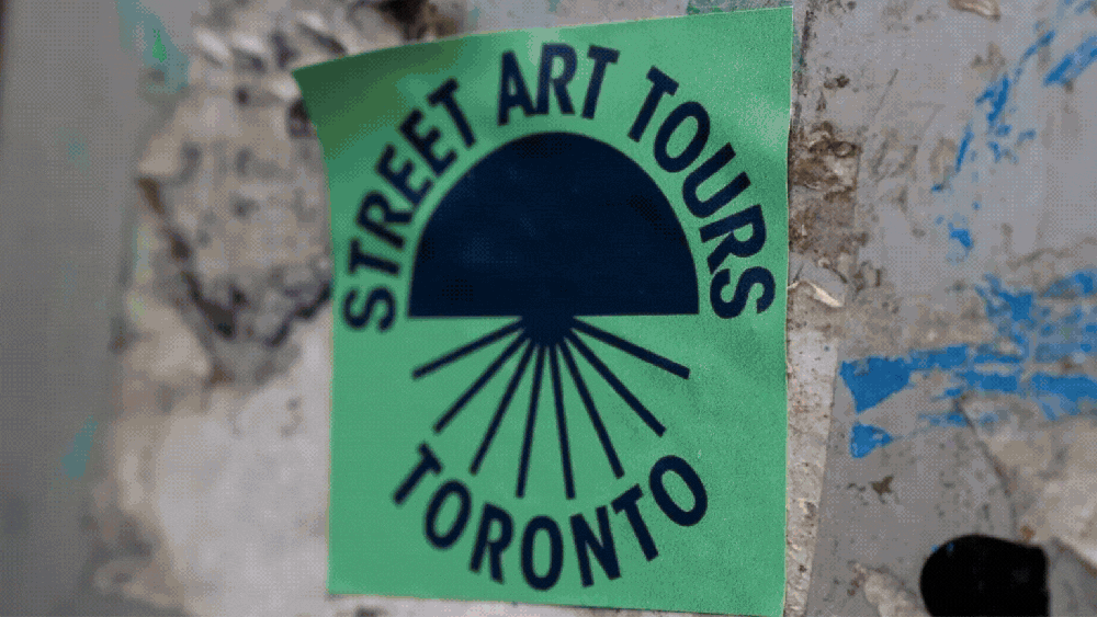 Sticker reading 'Street Art Tours Toronto' with sun graphic on a textured surface.