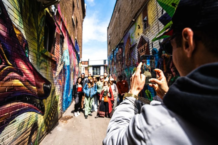 Person photographing colorful mural alley with group posing.