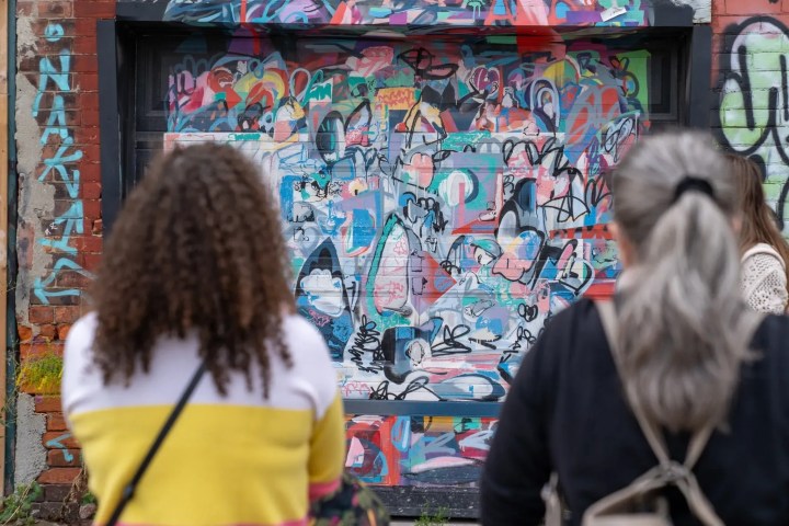 Two people observing colorful graffiti on a brick wall.