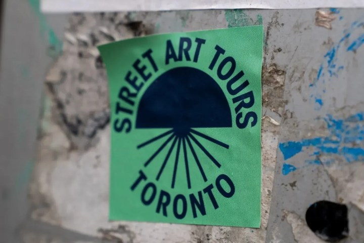 Green sticker on wall reading 'Street Art Tours Toronto' in blue letters with a sunburst design.